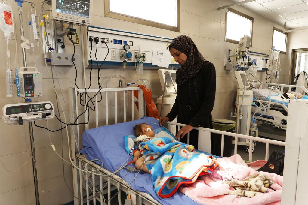 Balqees Abu Ajwa, madre de Sama Abu Ajwa, de ocho meses, está de pie junto a la cama de su hija, que está hospitalizada y sufre insuficiencia renal aguda.